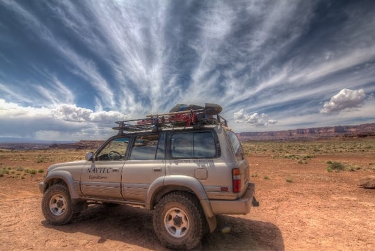 A silver NAVTEC SUV parked in Arches National Park with a dark cloudy sky moving overhead.