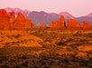 Red rock formations and natural arches in the desert landscape, with distant mountains in the background under a pinkish sky.