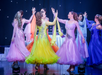 Dancers in colorful, flowing dresses perform on stage under star-like lights.