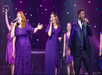 Performers in sparkly purple outfits singing on stage with microphones, while background performers hold tambourines.