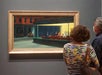 Two people view Edward Hopper’s painting “Nighthawks” displayed in a museum gallery.