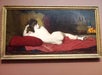 A framed painting of a nude woman lying on her side on red cushions, with draped fabrics, a brass vessel, and a bowl of oranges in the background.