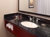 A bathroom vanity with a black countertop, a sink, rolled white towels, toiletries, a large mirror, and a framed wall art in the background.