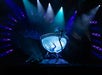 A performer is submerged in a large, water-filled tank shaped like a goblet on a stage with dramatic blue and purple lighting effects.