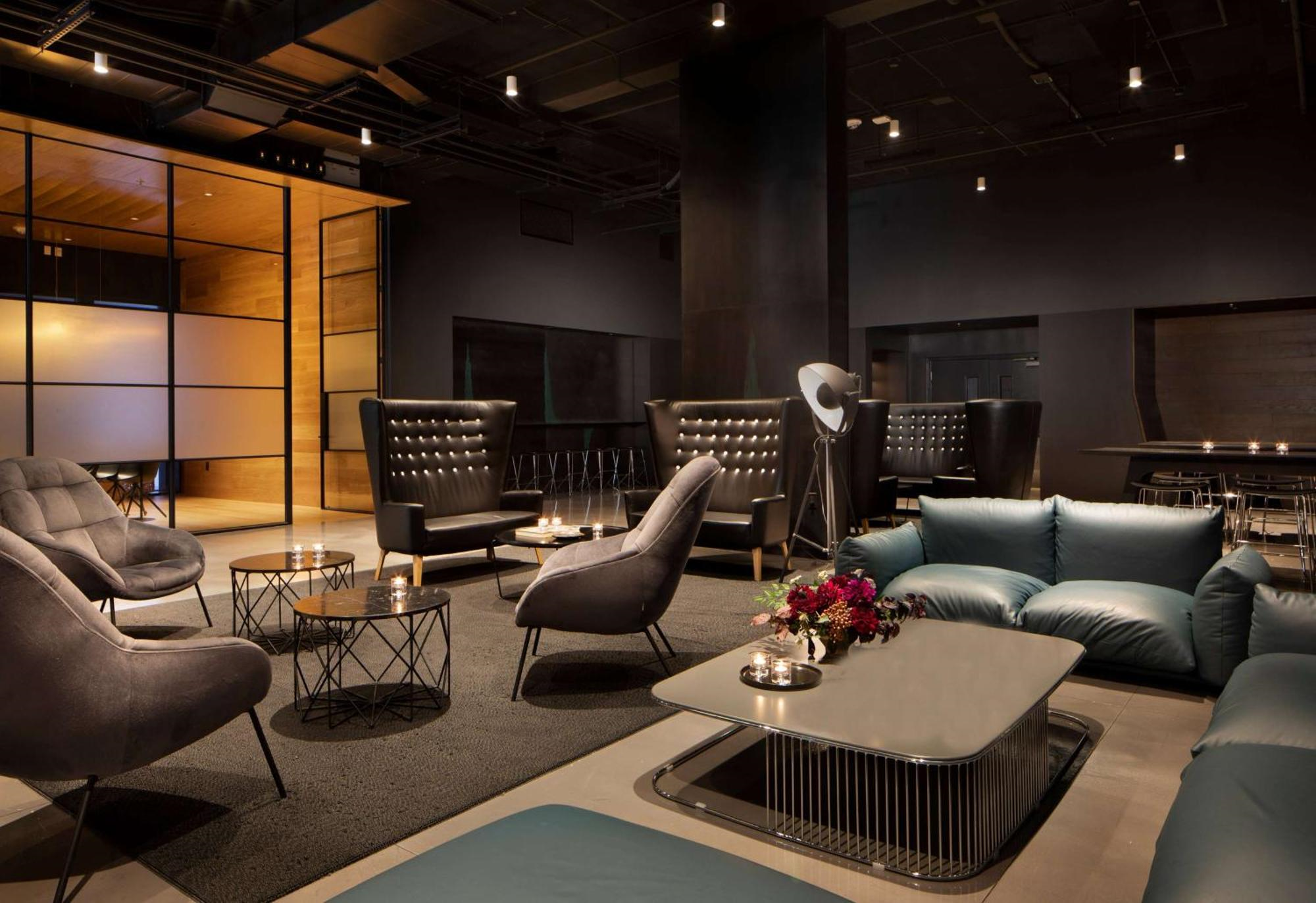 Modern lounge with sleek armchairs, high-back chairs, low tables, and subdued lighting; dark color palette with minimal decor and contemporary furnishings.