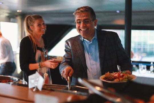 Two guests smiling and plating their food at the buffet on the Baltimore Dinner Cruise in Baltimore, Maryland