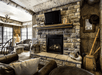 A rustic hunting themed sitting area leather and wooden furniture, a large stone fireplace, a TV, and large windows on the far left walls.