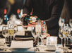 A sever wearing all black pouring glasses of white wine on a table filled with plates and glasses on the Bateaux New York Premier Brunch Cruise.