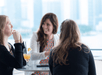 Women sitting at a table enjoying cocktails and chatting on the Bateaux New York Premier Brunch Cruise with the city in the distance.