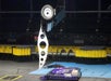 A robot battle scene with one robot flipped vertically using a metal lifting arm, while another robot lies flat on the arena floor.
