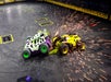 Two small combat robots clash, producing sparks on an arena floor. Both robots have colorful designs; one is purple and green, and the other is yellow and black.