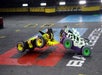 Two combat robots collide mid-air in an arena, with sparks flying. They have colorful designs on a marked floor labeled "BATTLEBOTS.