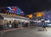 People walking outside the entrance of a BattleBots event tent at night, with Las Vegas buildings lit up in the background.