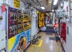 A brightly lit submarine corridor with control panels, colorful signage, and safety equipment lining the walls.
