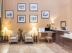Hotel lobby with two armchairs, a side table with a vase and lamps, a desk with a computer, a printer, and framed black-and-white photos on the wall.