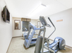 Small gym room with two elliptical machines, a treadmill, a wall-mounted TV, and a window with blinds.