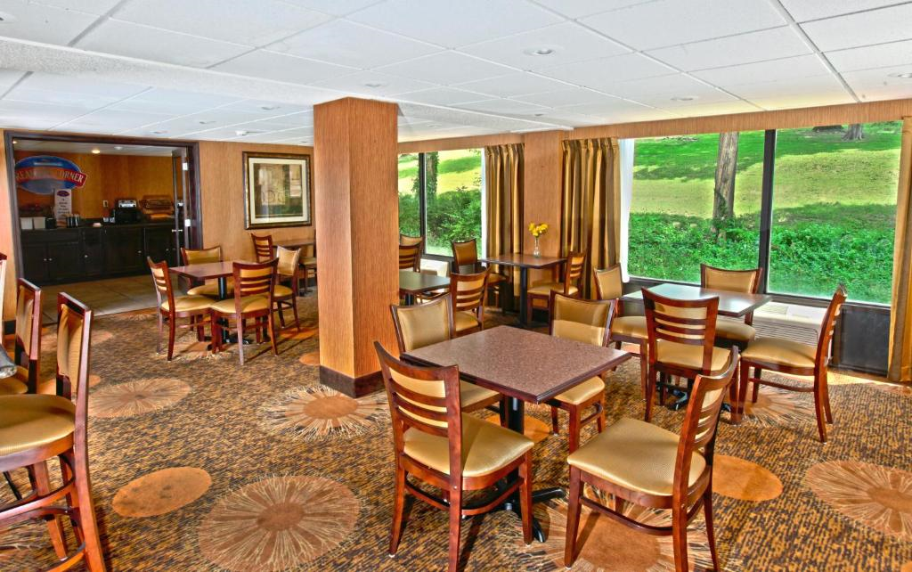 A small dining area with wooden tables and chairs, carpeted floor, and large windows showing a green landscape outside.