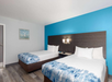 Hotel room with two double beds with blue and white bedding, a dark wood headboard, a blue accent wall, modern wall lights, a small nightstand with a phone, and a framed picture on the wall.