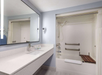 A modern bathroom with a large mirror, sink, and toiletries on the countertop. A shower and bathtub with a shower curtain and safety rails are on the right.