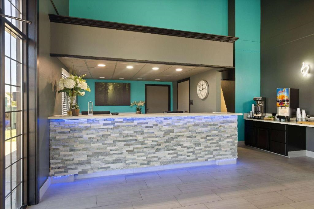 A reception area with a stone-patterned front desk, modern decor, a wall clock, beverage station, and teal and gray walls.