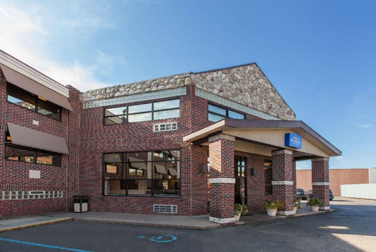 Brick building exterior with large windows and a covered entrance, set against a clear blue sky.