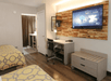 Hotel room with two beds, a desk with a chair, wall-mounted TV, and wood panel accent. A door leads to the bathroom, and curtains cover a window.