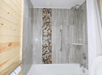 Bathroom with a bathtub and shower, featuring a pebble stone strip on the gray tile wall. A metal grab bar is installed beside the shower fixtures.