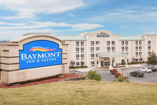 Entrance to the hotel with the hotel sign and ample outdoor parking space.
