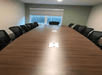 A long dark brown table lined with black office chairs in a meeting room with a window on the far wall at Baymont by Wyndham.