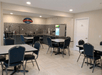 A dining room with with gray tables and blue chairs and a breakfast bar with gray cabinets and stone work on the back wall.