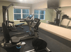A small fitness center with a couple pieces of cardio equipment and a weights machines in front of a large mirror and a window on the far wall.