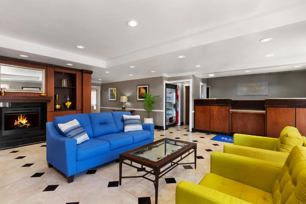 Hotel lobby with a blue sofa, two yellow chairs, a glass coffee table, and a fireplace. Black and white patterned floor. Reception desk in the background.