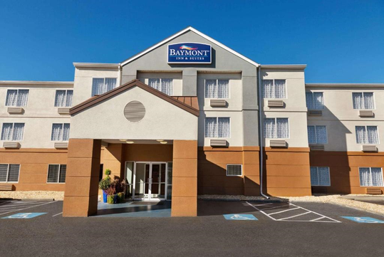 Front view of Baymont Inn & Suites hotel with beige and brown facade, large entrance, multiple windows, and disabled parking spots in the foreground.