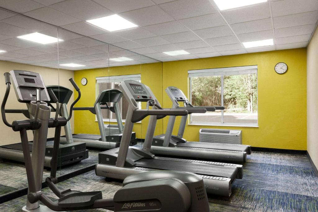 Small gym with three treadmills facing mirrors, yellow accent wall, window with outdoor view, and wall clock.