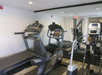 A gym room with treadmills, an exercise bike, and an elliptical machine facing a large mirror.