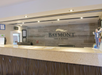 Hotel front desk with the Baymont Inn & Suites logo on the wall, featuring a textured counter and wooden paneling.