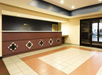 Hotel lobby with a tiled floor, a reception desk with decorative panels, soft lighting, and a sliding glass door entrance.