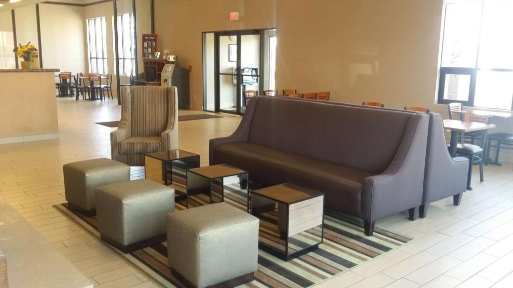 Hotel lobby with brown sofa, striped armchair, four square ottomans, and small tables on a striped rug. The background shows dining tables and large windows.