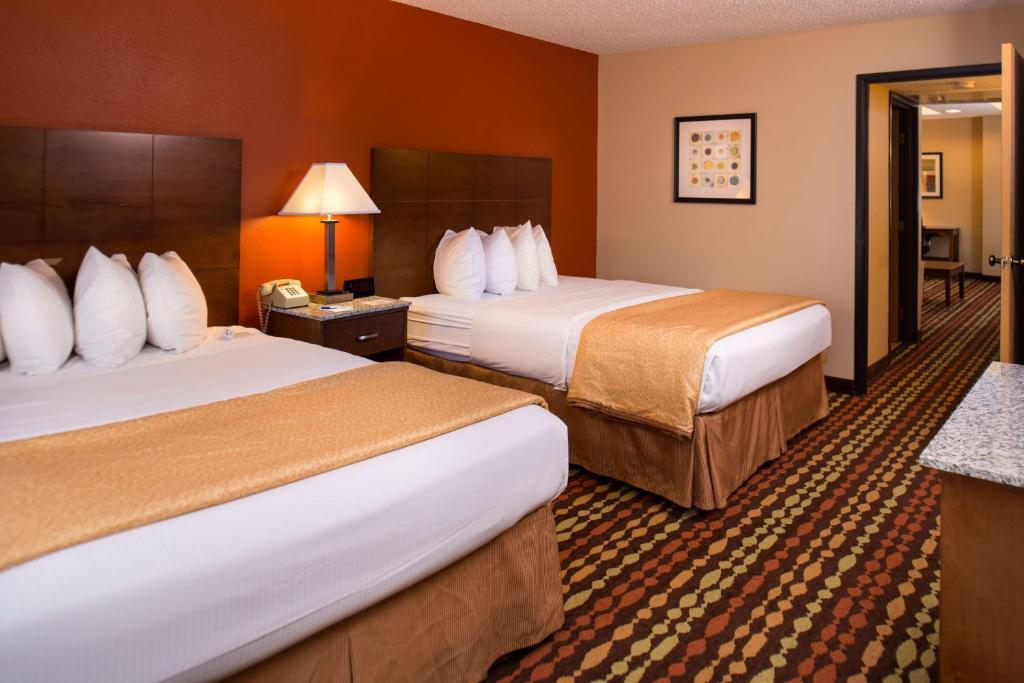 Hotel room with two double beds, white bedding, a nightstand with a lamp, patterned carpet, and a picture on the wall.