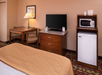 Hotel room with a table and chairs, flat-screen TV on a dresser, and a mini-fridge and microwave on a wooden stand.