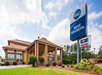 Exterior view of a Best Western hotel with a large sign, surrounded by greenery and a cloudy sky.