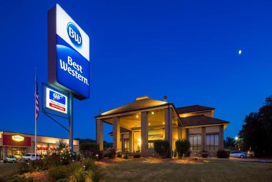 Exterior view of a Best Western hotel at dusk, with illuminated signs and a clear sky in the background.