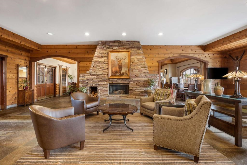 A cozy lounge with four upholstered chairs and a round table in front of a large stone fireplace, set in a wooden-paneled room.