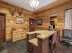 A rustic reception area with a wooden counter, deer antlers on the wall, a chandelier, and two leather chairs.