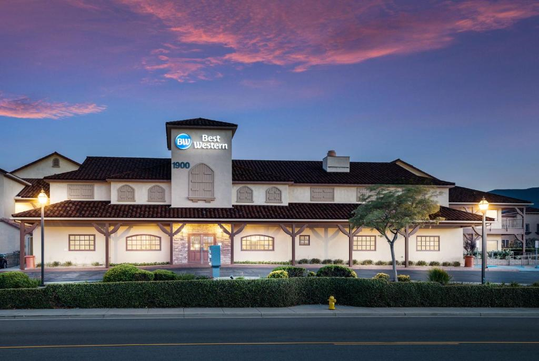 A two-story Best Western hotel building with exterior lights on at dusk, featuring a red tiled roof and a large sign on the front facade.