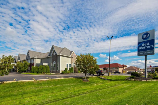 Exterior view of the Best Western hotel with a parking lot and grassy area under a partly cloudy sky.