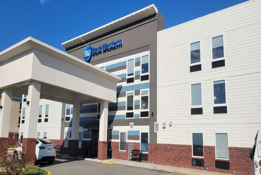 Exterior view of a Best Western hotel with a blue sky background, featuring a covered entrance and multiple windows.