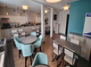 A modern dining area with round and rectangular tables, chairs, and a buffet section with beverages and food items. Neutral and teal-colored decor.