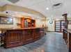 An empty hotel lobby with a wooden reception desk, tiled ceiling, wall art, and a door. Social distancing markers on the floor.