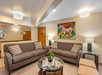 Lobby area with two brown sofas around a glass coffee table, a vibrant horse painting on the wall, and modern lighting fixtures.